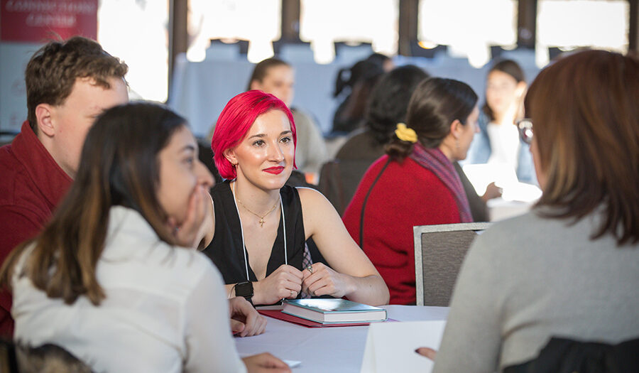 Students sitting at table and talking to alumna