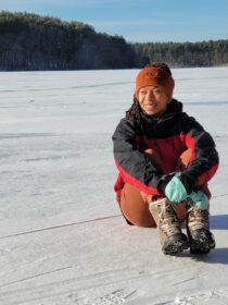 Olivia Barksdale '19 sits on an ice-covered lake. Winter 2022, Middlesex Fells Reservation, Massachusetts.