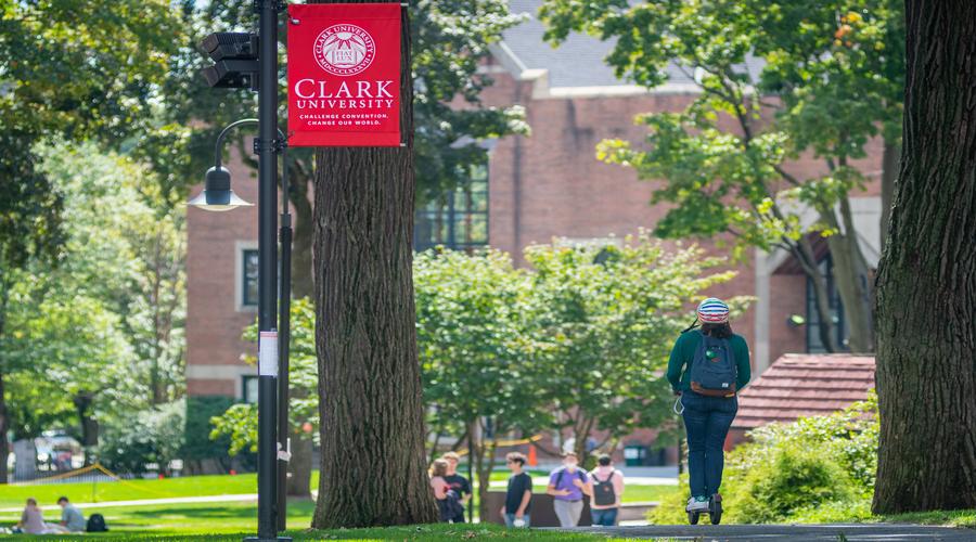 Student rides on scooter through the green.