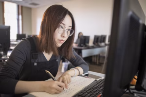An accounting student takes notes in front of a computer monitor