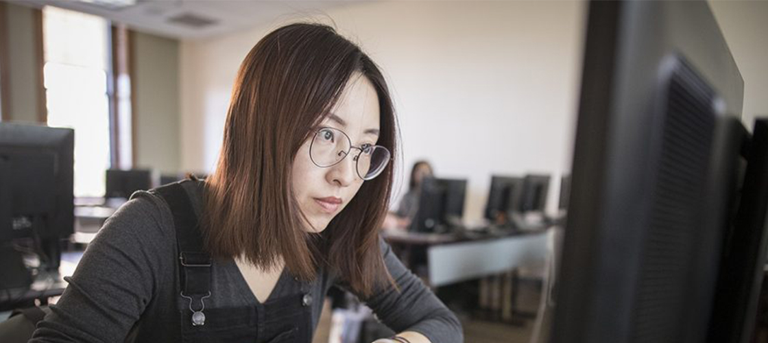 Student with notepad and pen looking at computer screen