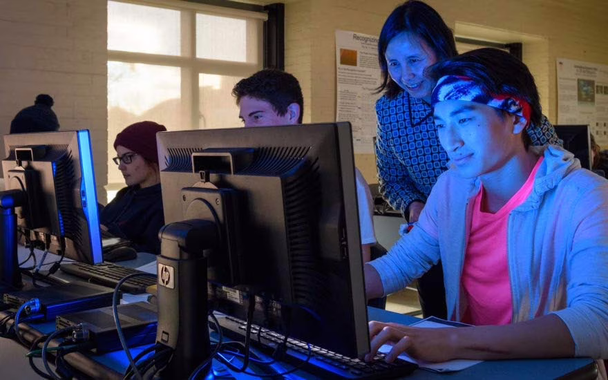 A professor watches as students work in a computer lab