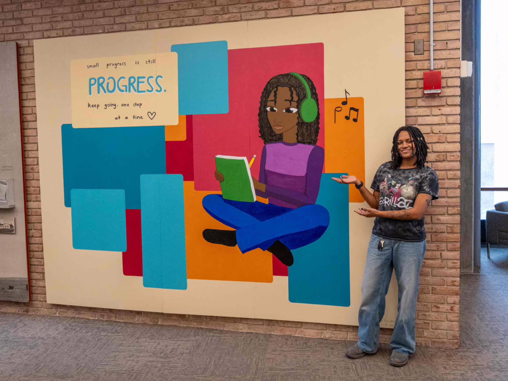 Skye Donaldson ’26 standing beside her mural in the Goddard Library, Clark University