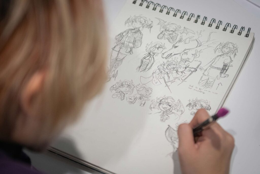 A student draws character designs by hand in a sketchbook