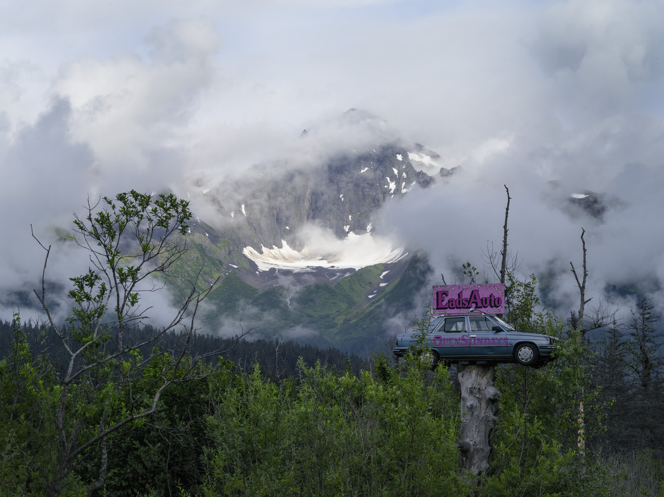 mountain in the clouds with a car stuck in a tree nearby