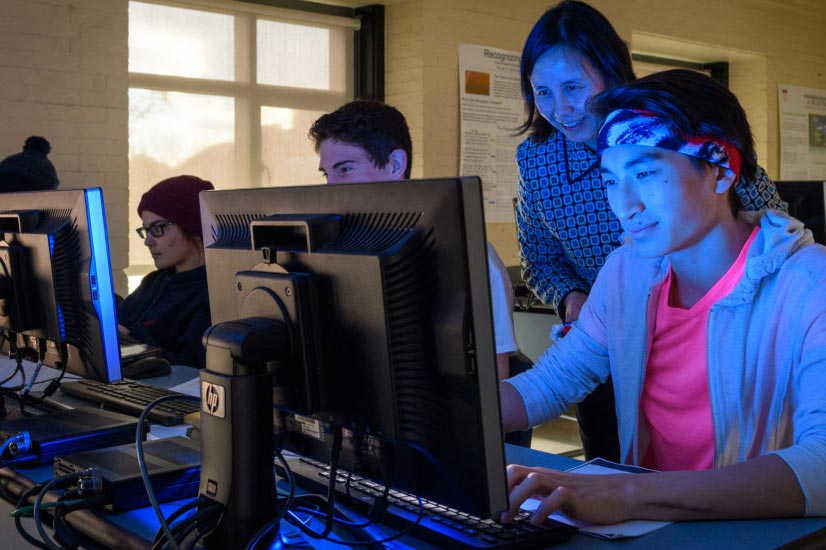 A professor leaning over to survey student work in a computer science class