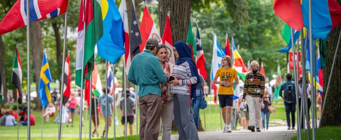 Move-in Day at Clark University is a welcome for families all over the world. A family stands talking on a pathway lined with international flags