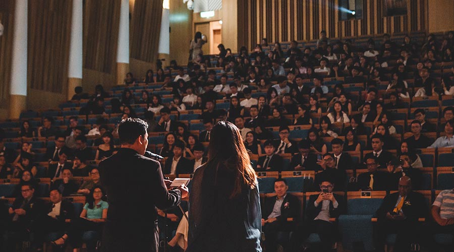 Two scholars standing before an auditorium of people