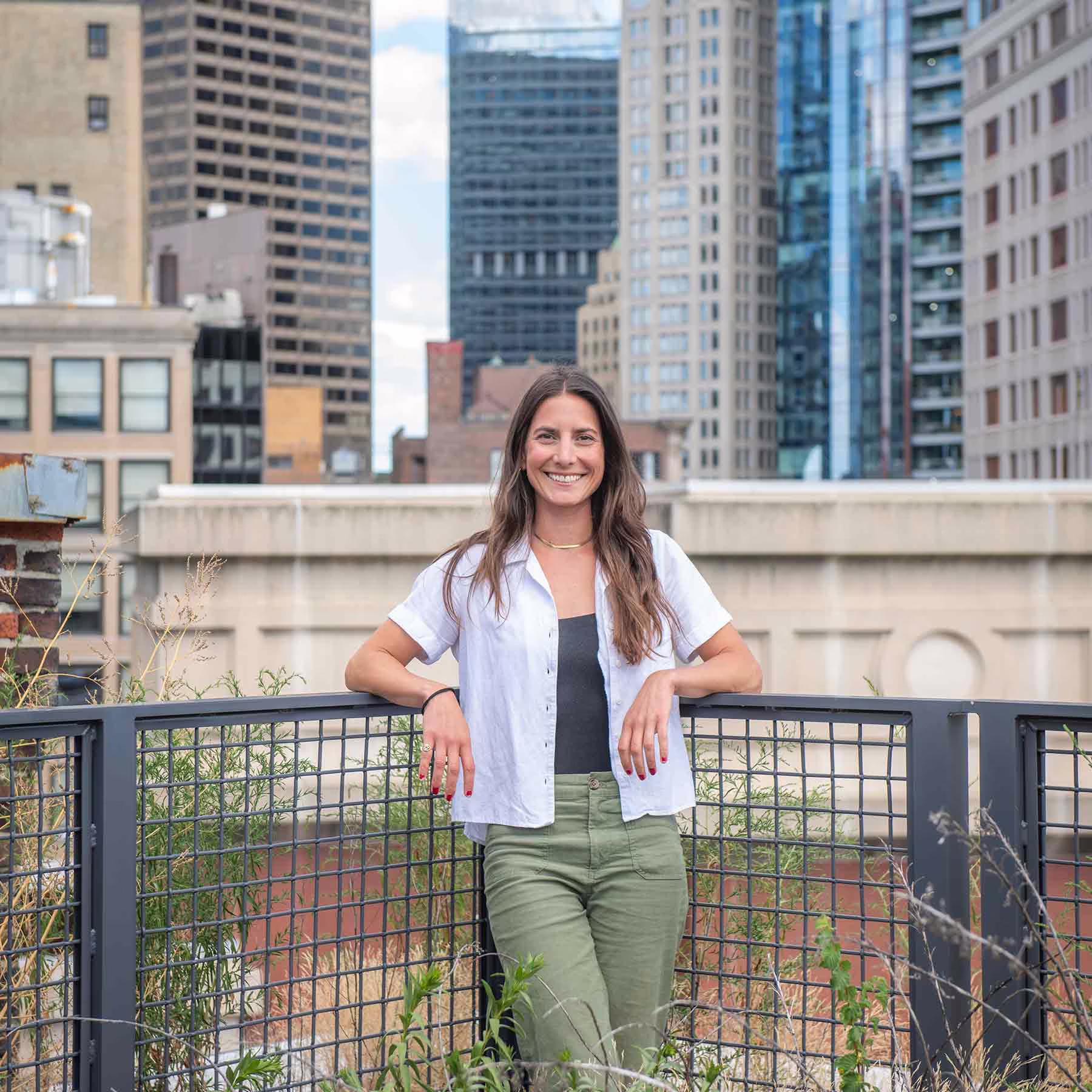 Serena Galleshaw ’12 standing in an urban green space with a city skyline in the background