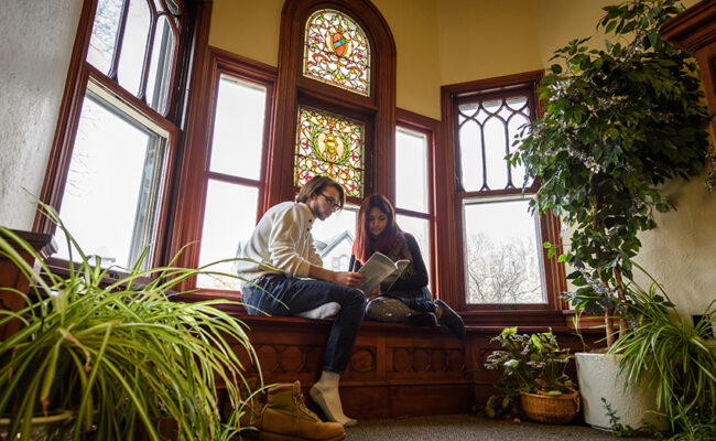 Anderson House - students sitting on bench with stain glass over them