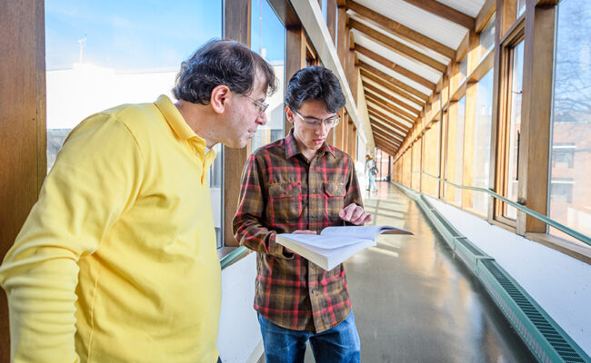 teacher mentoring student in long hall in the math physics building