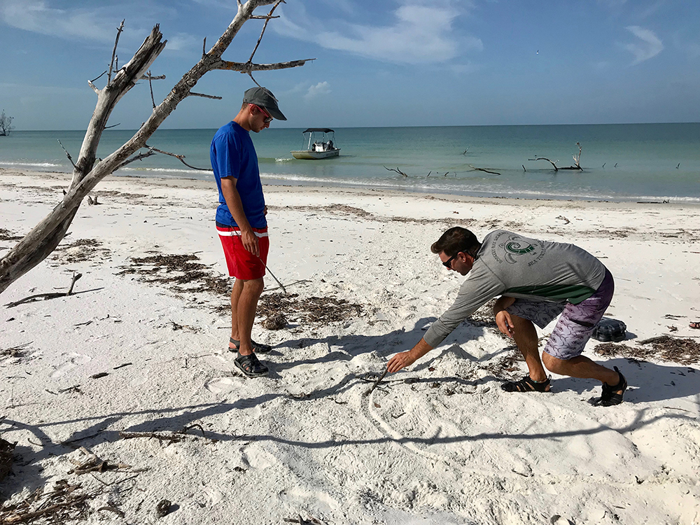 two men in beach sand drawing a line in he sand