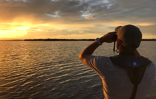 man looking into binoculars of lake