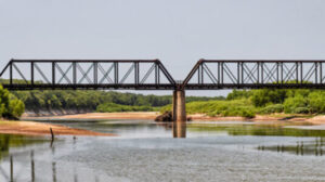 A railway trestle crossing the Red River between the U.S. states of Texas and Oklahoma on a bright summer afternoon.