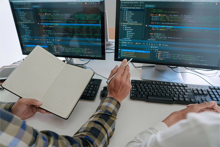 Student with notebook pointing at computer with code