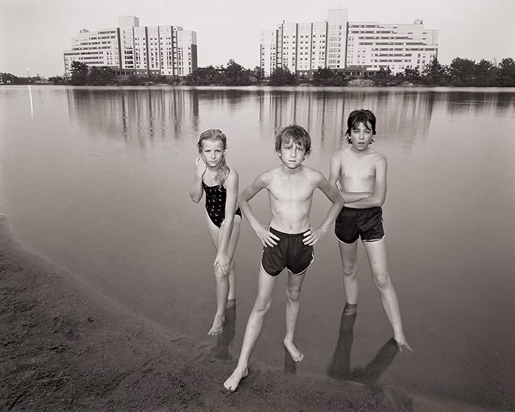 Three children stand at the edge of Bell Pond with apartment blocks visible across the pond behind them, 1983