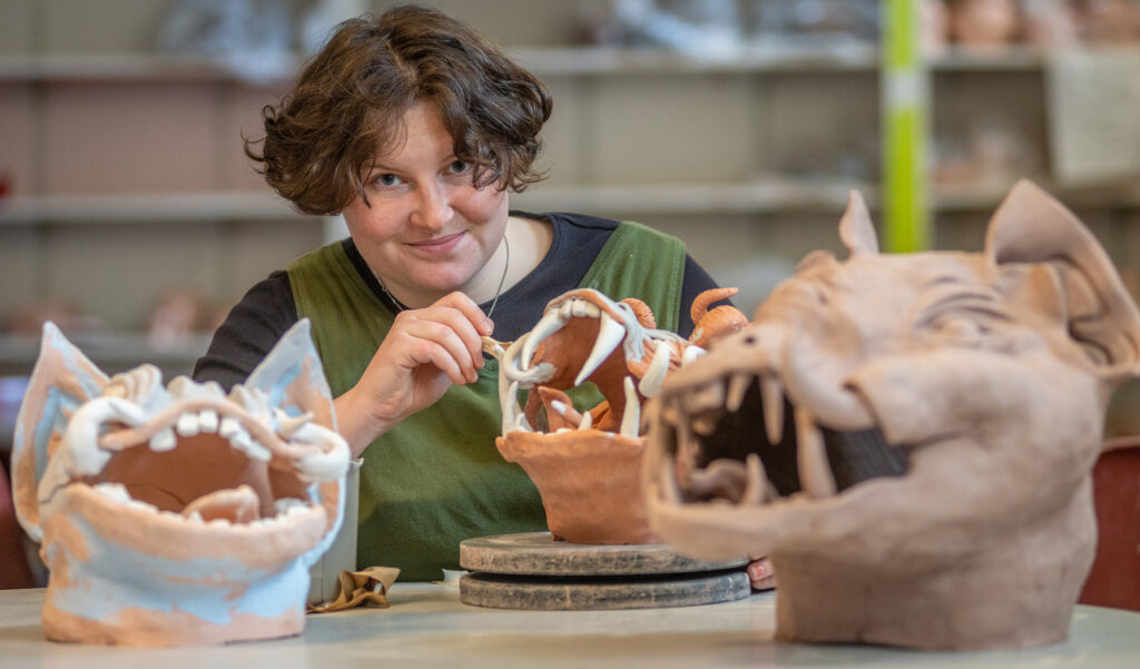 Brynn Kevin working on a clay dragon in an art studio