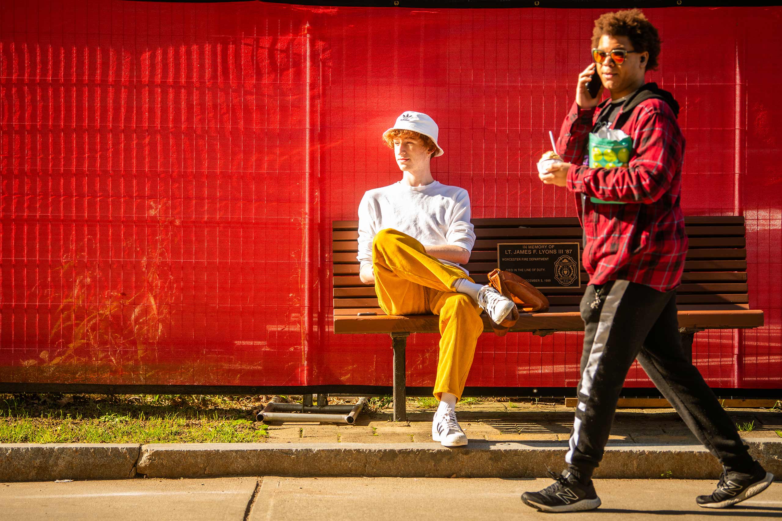 A student sitting on a bench as another walks by on #FreshCheckDay, Clark University