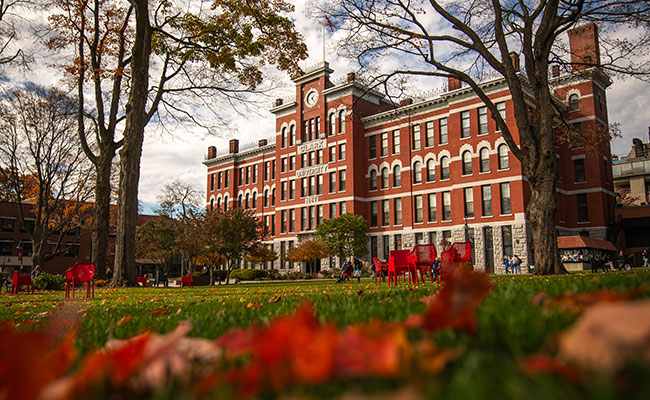 A close-up of fall leaves on grass in the foreground with Jonas Clark Hall in the distance