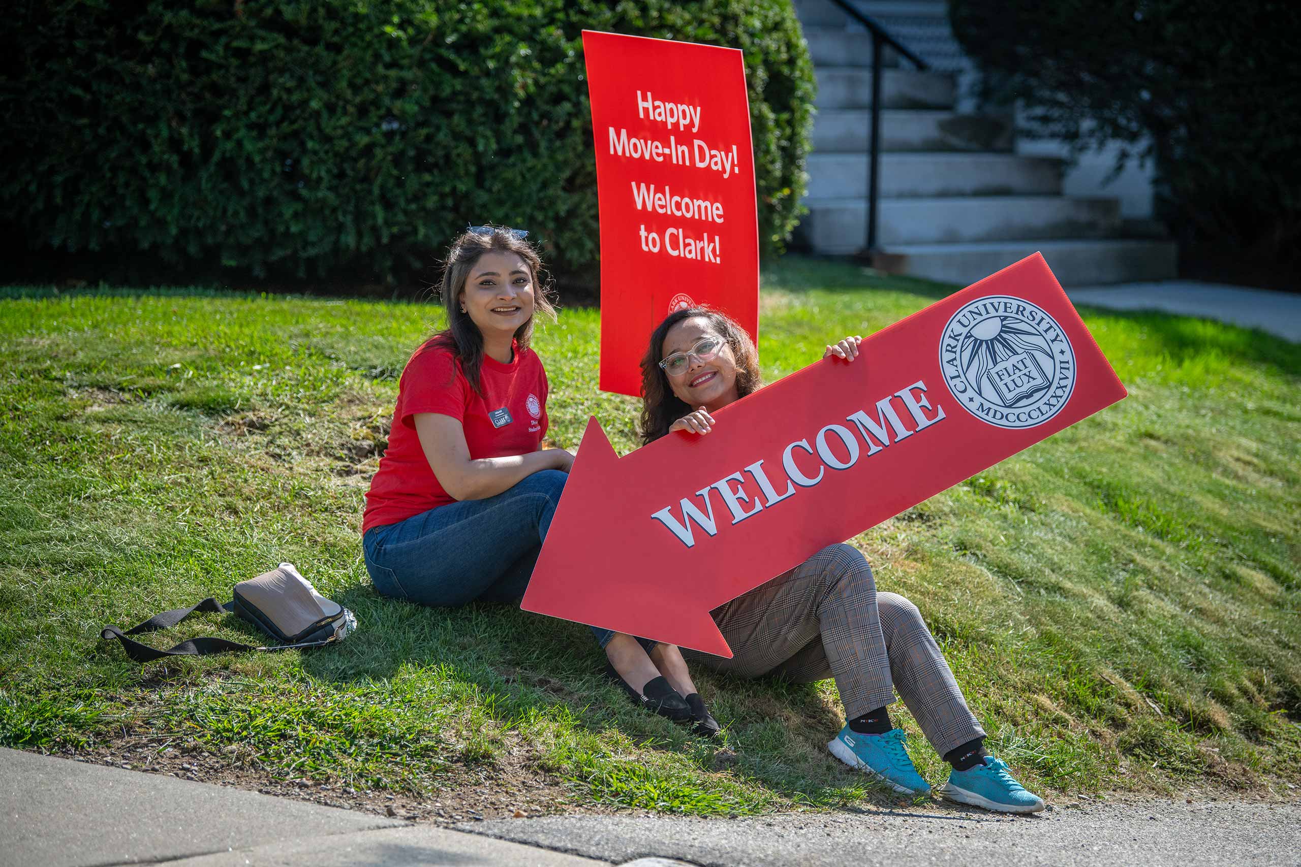 Two people sitting on the grass, holding a welcome sign