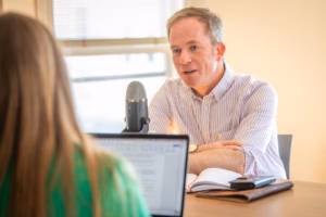 man sitting at table talking into podcast microphone