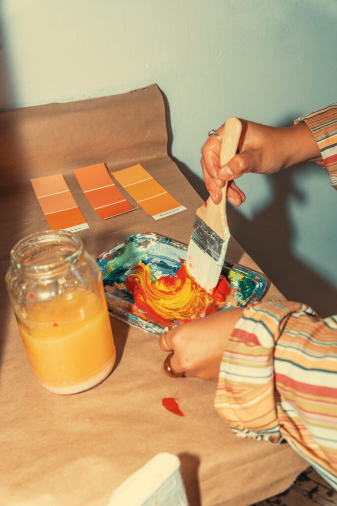 a woman holds a paintbrush with orange and yellow hues