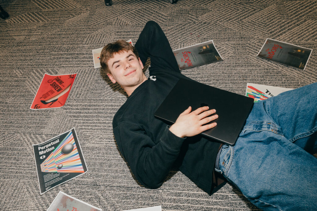 student lays on floor with laptop and papers