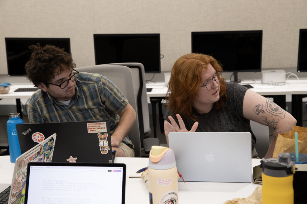 two people sit at table with laptops
