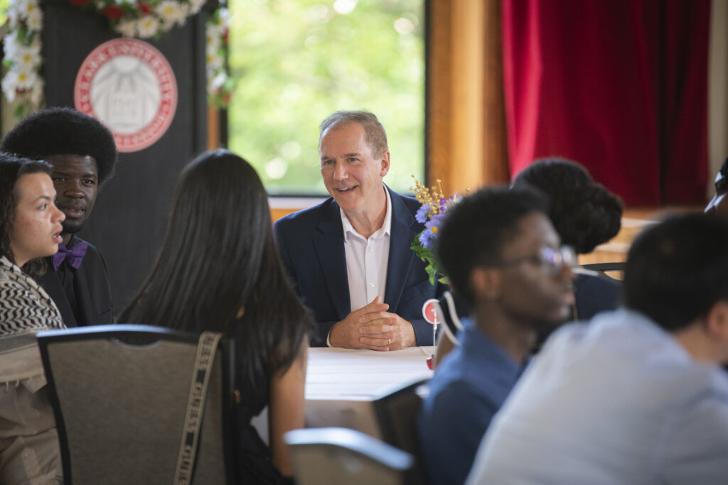 university president sits with students at table