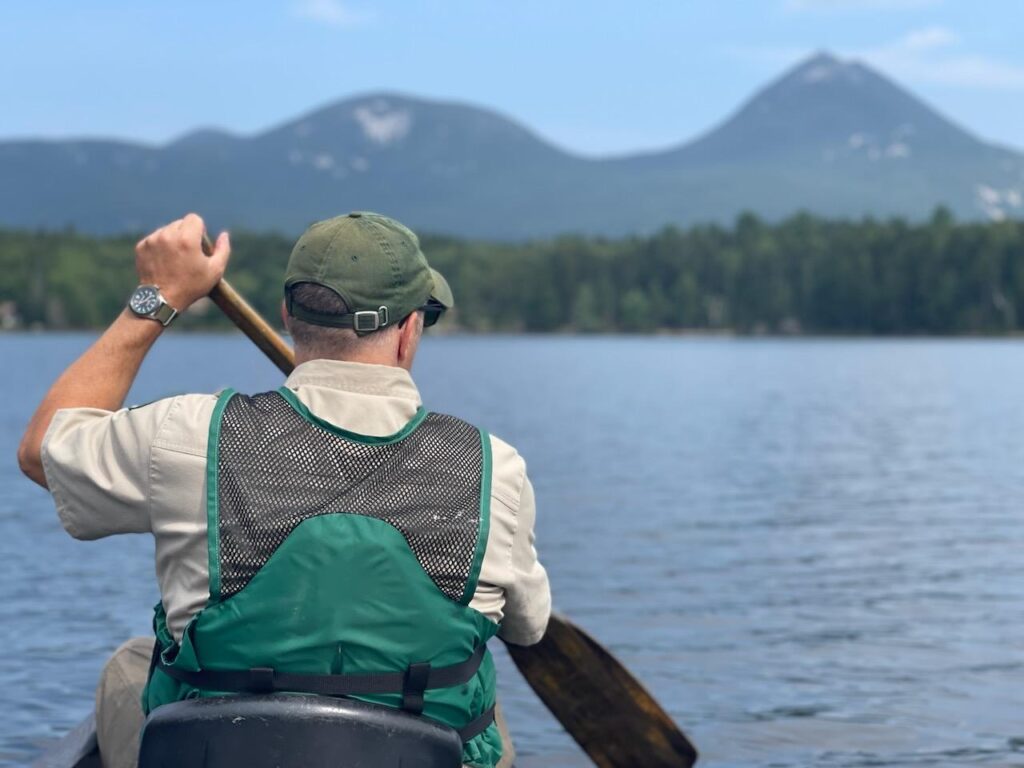 man padding canoe on lake surrounded by mountains