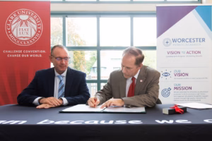 Clark University President David Fithian signing a memorndum of understanding while sitting next to Worcester Public Schools Superintendent Brian Allen.