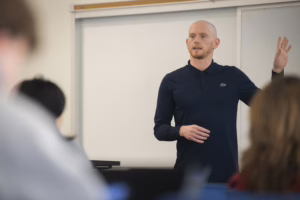 professor stands in classroom talking to students