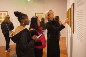 professor points at art print in museum while talking with two students