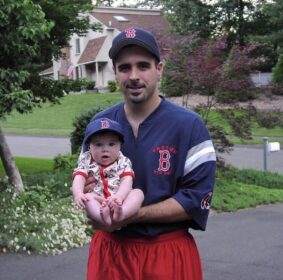 Dad holding infant girl in Red Sox onesie