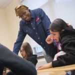 student helps younger student at desk