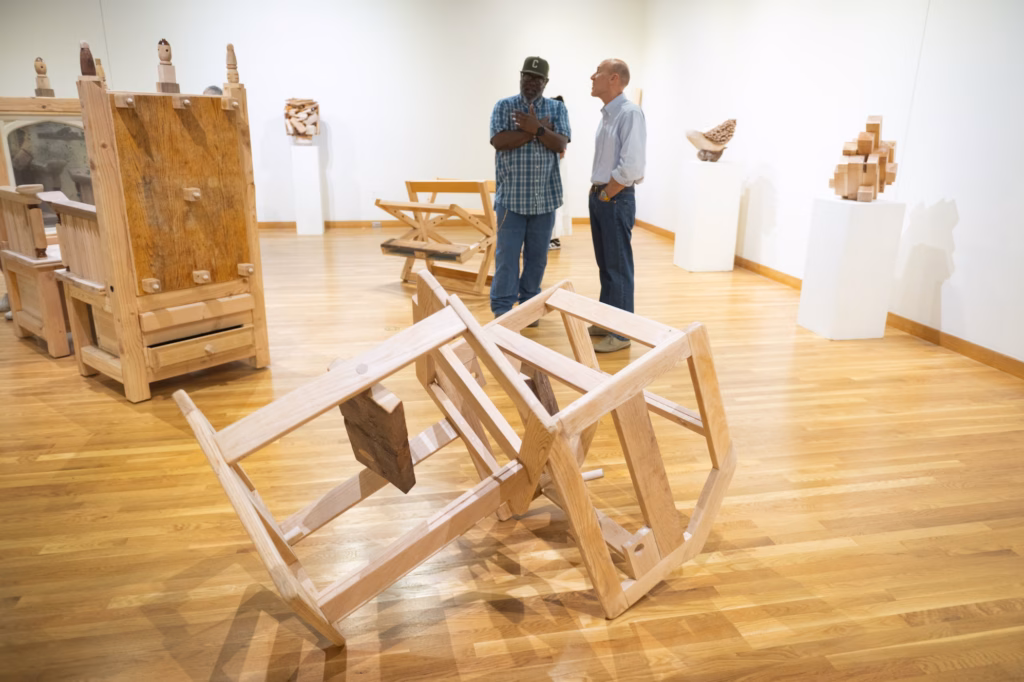 wooden art piece in gallery with two people standing nearby
