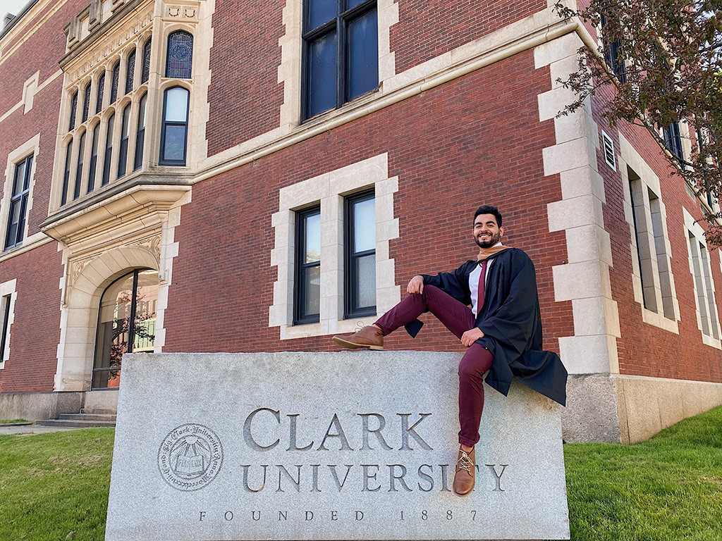 Matheus Goncalves sits on the Clark University sign outside campus