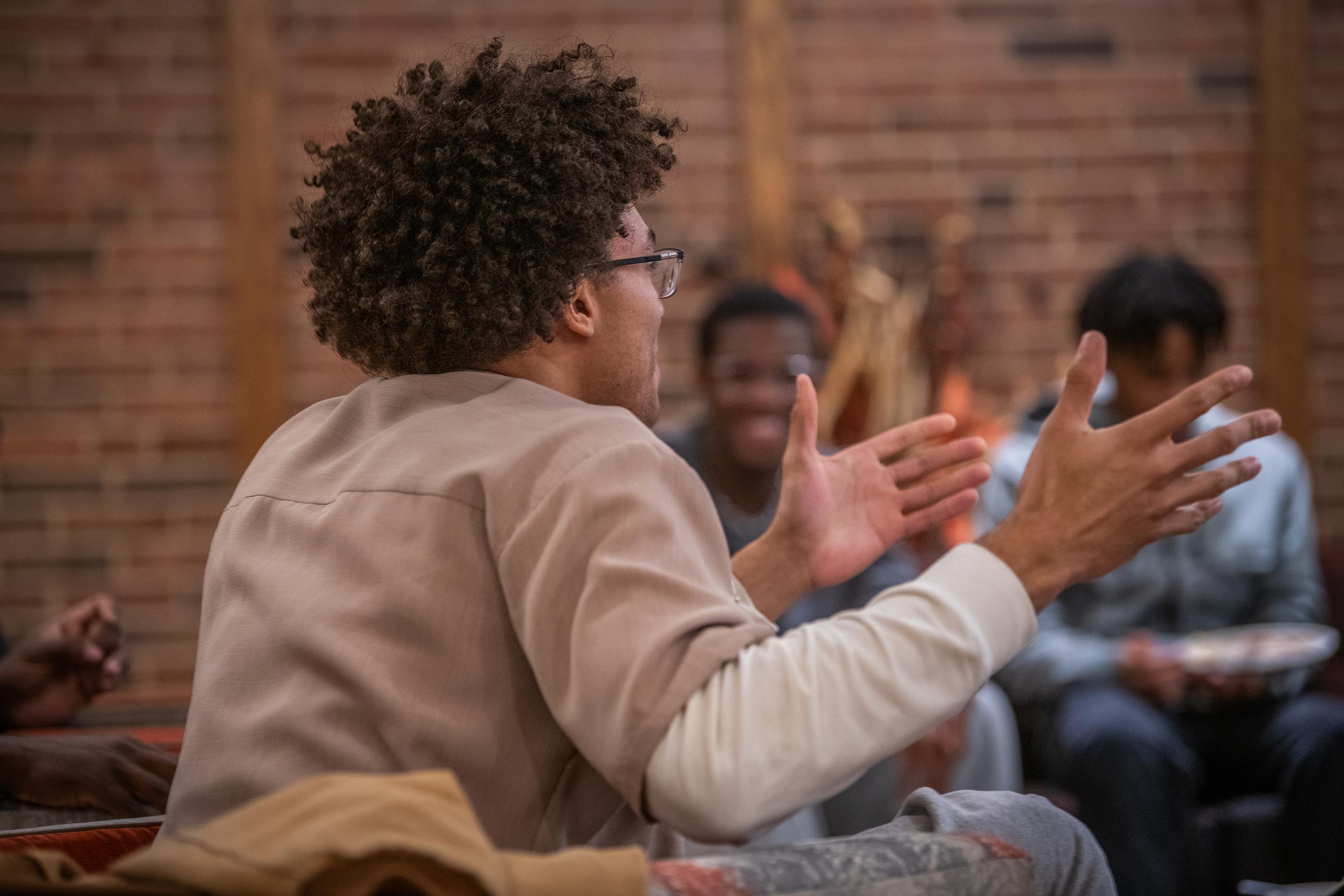 Aedan Derrick ’26 seen from the back speaks while gesturing before a group of members of the Men of Color Alliance, who smile in the background