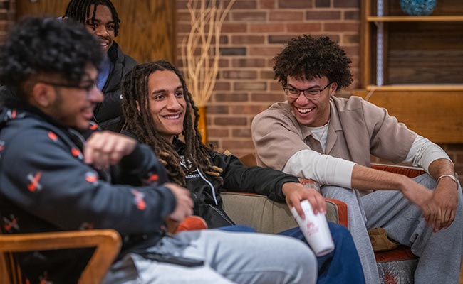 A group of students laughing and smiling during a gathering event of the Men of Color Alliance at Clark University