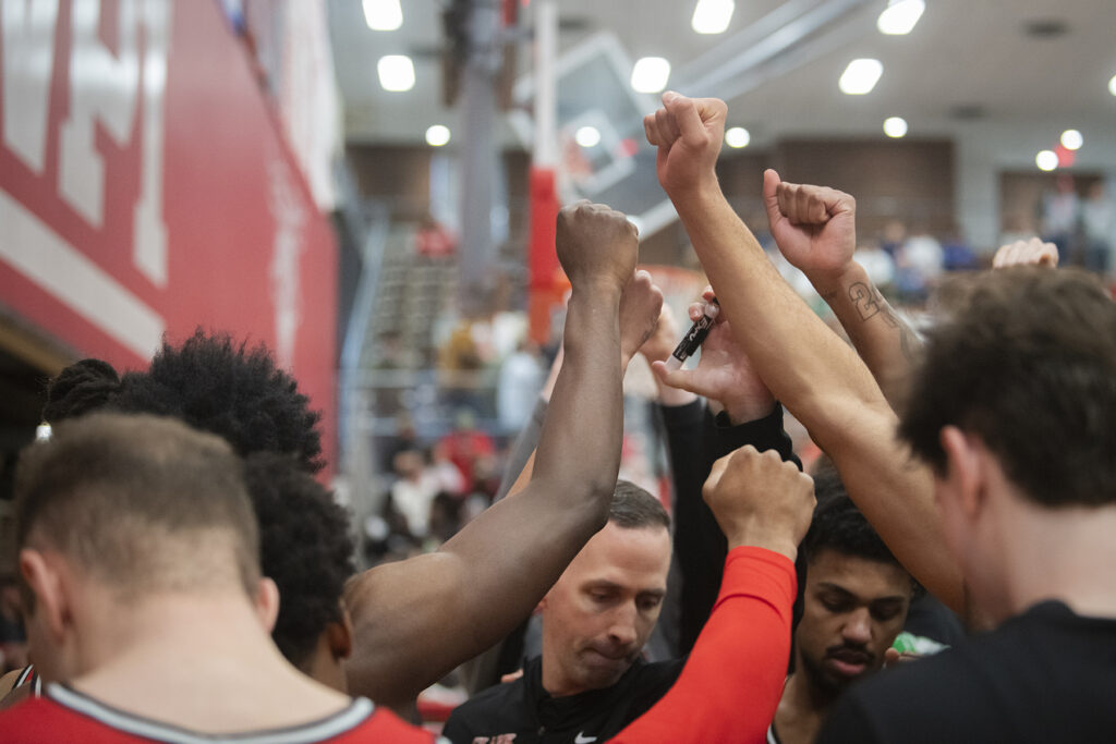 Clark University men's basketball team members raise fists during time out huddle in 2025 NEWMAC championship game