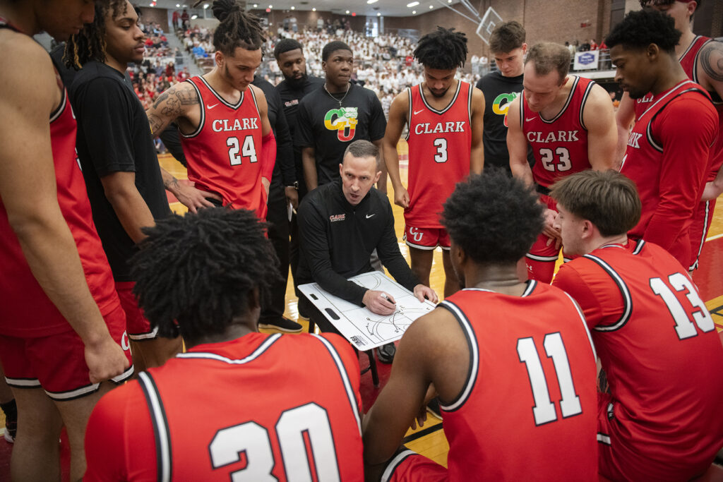 Coach Tyler Simms with Clark University men's basketball team players during a time out in 2025 NEWMAC championship game