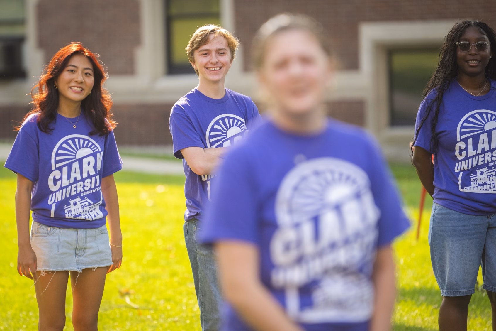 four students in purple T-shirts on campus green