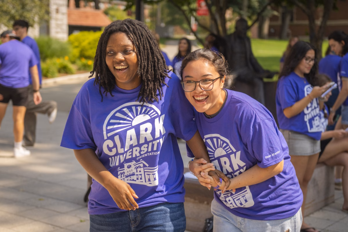 two students in purple T-shirts laughing on campus