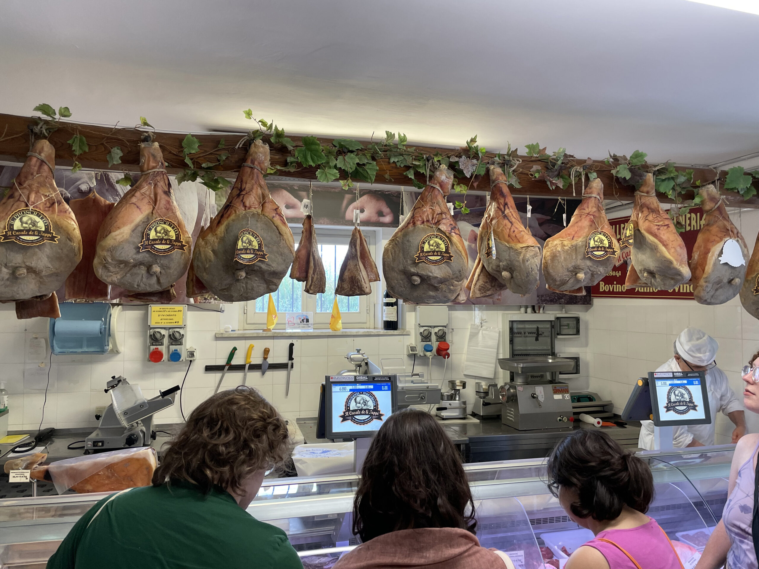 Students visiting salumi shop with hams hanging above