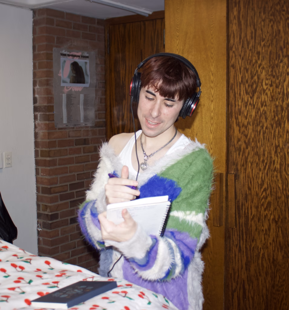 student in green, blue, and purple sweater writing in notebook