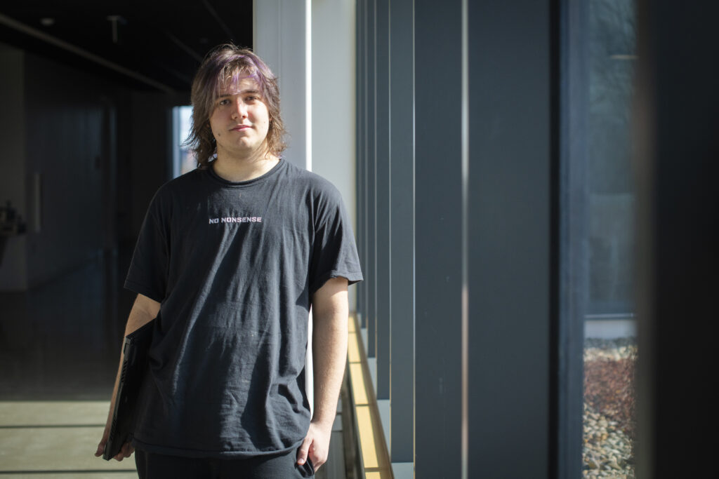 student stands in hallway with laptop