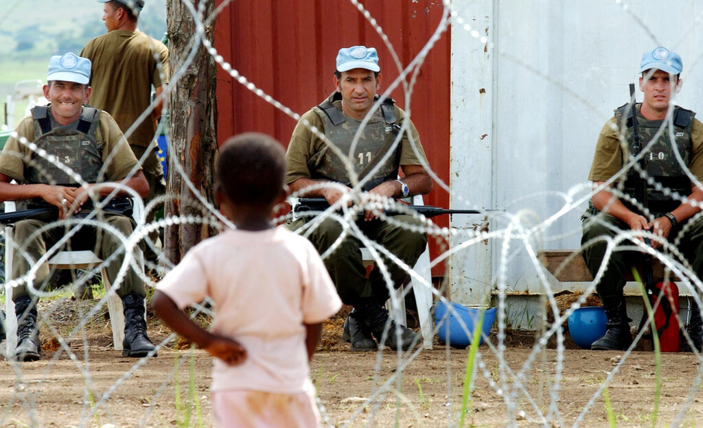 A young boy looks through concertina wire at three United Nations peacekeepers at a refugee camp in Bunia, Democratic Republic of Congo, following a wave of ethnic killings.