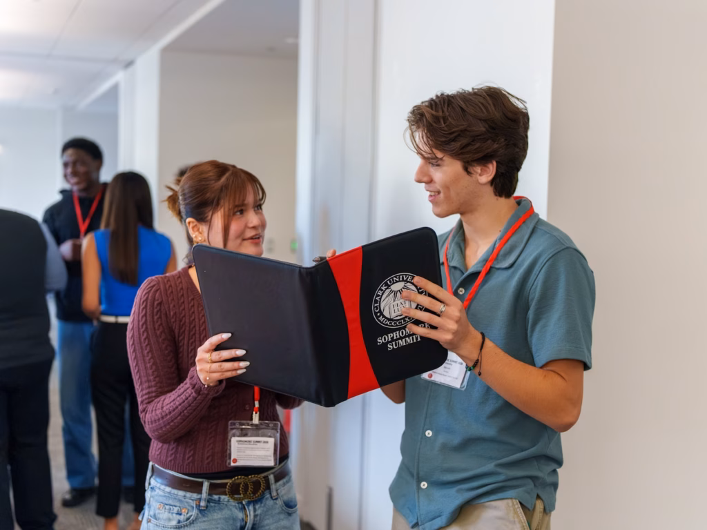 two students talk while holding open a workbook