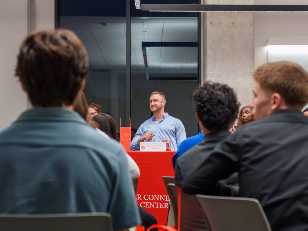 at center, alumni sits at table talking to room full of students