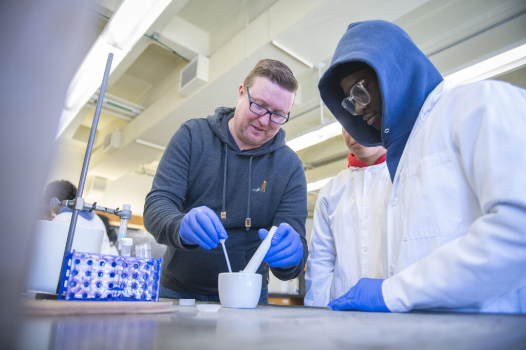 Professor Don Spratt shows a student from North High School how to grind cellular material with a mortar and pestle.